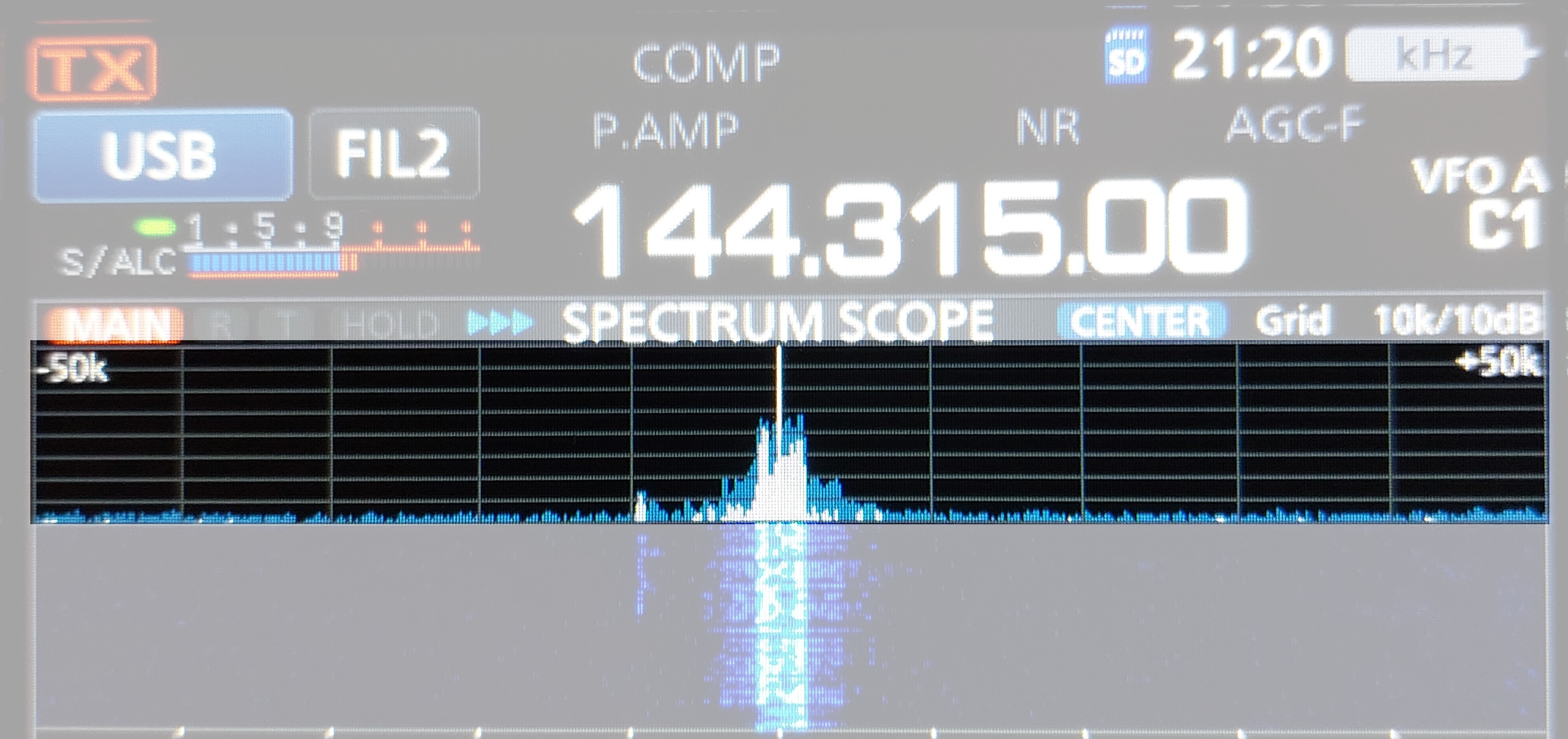 1) Kurzbeschreibung: Display eines Funkgerätes mit Frequenzanzeige „144.315.00“, Spektrums- und hervorgehobene Wasserfalldarstellung eines starken Signals in der Mitte.

2) Ausführliche Beschreibung: Die Abbildung zeigt das Display eines Funkgerätes auf schwarzem Untergrund. Neben weiteren Beschriftungen steht in der Mitte in großen, weißen Ziffern die Frequenz „144.315.00“. Darunter ist in blauer Farbe die Anzeige des Spektrums um die eingestellte Frequenz zu sehen, die von den Angaben „–50k“ (links) und „+50k“ (rechts) begrenzt wird. In der Mitte gibt es einen schmalen, hohen Peak mit kleineren Flanken. Darunter befindet sich ein Wasserfalldiagramm auf dunkelblauem Hintergrund mit einer hellblau-weißen vertikalen Spur unterhalb des Peaks. Die Darstellung des Spektrums ist hervorgehoben, der Rest der Abbildung ist abgeblendet.