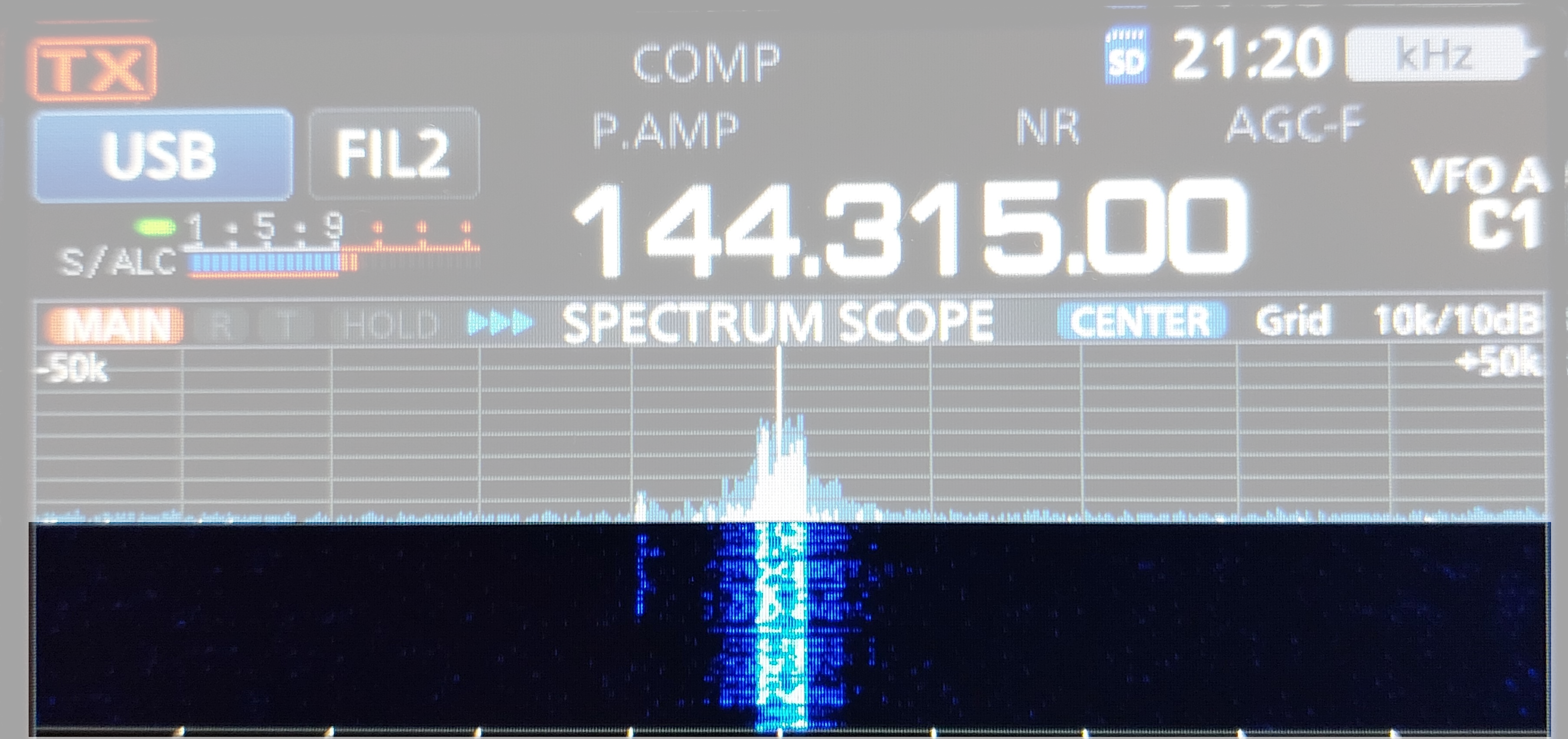 1) Kurzbeschreibung: Display eines Funkgerätes mit Frequenzanzeige „144.315.00“, Spektrums- und hervorgehobene Wasserfalldarstellung eines starken Signals in der Mitte.

2) Ausführliche Beschreibung: Die Abbildung zeigt das Display eines Funkgerätes auf schwarzem Untergrund. Neben weiteren Beschriftungen steht in der Mitte in großen, weißen Ziffern die Frequenz „144.315.00“. Darunter ist in blauer Farbe die Anzeige des Spektrums um die eingestellte Frequenz zu sehen, die von den Angaben „–50k“ (links) und „+50k“ (rechts) begrenzt wird. In der Mitte gibt es einen schmalen, hohen Peak mit kleineren Flanken. Darunter befindet sich ein Wasserfalldiagramm auf dunkelblauem Hintergrund mit einer hellblau-weißen vertikalen Spur unterhalb des Peaks. Das Wasserfalldiagramm ist hervorgehoben, der Rest der Abbildung ist abgeblendet.