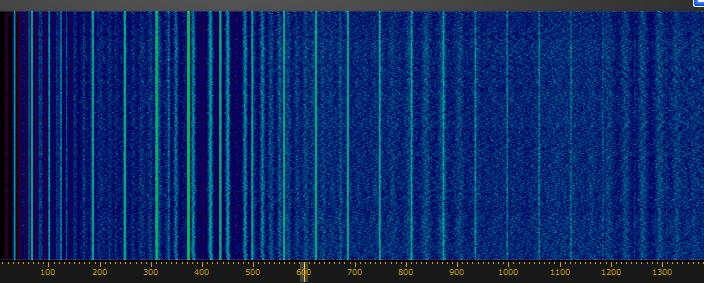 Dieser Alt-Text wurde noch nicht überprüft.

Zusammenfassung: Blaue Spektrums-/Wasserfallanzeige mit vielen schmalen, senkrechten hellen Streifen und einer gelb markierten Skala am unteren Rand.

Detaillierte Beschreibung: Das Bild zeigt eine rechteckige, farbcodierte Darstellung in überwiegend dunklen Blautönen mit körniger Textur. Über die gesamte Höhe verlaufen zahlreiche schmale, helle vertikale Linien in Cyan bis Türkis; sie sind links und im mittleren Bereich dichter und variieren in Helligkeit und Breite. Rechts sind die Linien insgesamt schwächer und teilweise regelmäßiger verteilt. Über die Breite liegen zusätzlich gleichmäßig verteilte, sehr feine vertikale Hilfslinien. Am äußersten linken Rand ist ein schmaler, dunkler Rot- bis Purpurstreifen sichtbar. Unten verläuft ein dunkler Balken mit gelben Markierungen und Zahlen von 0 bis 1300 (Einheit nicht angegeben); eine vertikale grüne Markierungslinie steht ungefähr bei der 600, weitere grüne Linien sind über die Breite verteilt. Insgesamt wechselt die Helligkeit in den blauen Flächen leicht, wodurch ein unruhiges, rauschähnliches Muster entsteht.