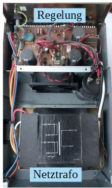 Dieser Alt-Text wurde noch nicht überprüft.

Zusammenfassung: Blick von oben in ein geöffnetes Metallgehäuse mit einer beschrifteten „Regelung“-Platine im oberen Bereich und einem großen, als „Netztrafo“ beschrifteten Transformator unten.

Details: Das Foto zeigt das Innere eines elektronischen Geräts in Hochformatansicht. Oben ist eine braune Leiterplatte mit mehreren schwarzen zylindrischen Elektrolytkondensatoren, Widerständen und weiteren Bauteilen montiert; darüber befindet sich ein hellblaues Textfeld mit der Aufschrift „Regelung“. In der Mitte sitzt ein kleiner schwarzer Lüfter mit rot-schwarzen Anschlussdrähten. Rechts daneben ist ein weiteres schwarzes, zylindrisches Bauteil an der Seitenwand befestigt. Entlang der linken Gehäuseseite verläuft ein Bündel mehrfarbiger Kabel (u. a. rot, gelb, blau, weiß). Unten nimmt ein großer schwarzer Transformator den Großteil des Platzes ein; auf seiner Oberseite ist ein vereinfachtes Anschluss-/Wicklungsdiagramm mit Linien und Zahlen (z. B. 0, 10, 12) aufgedruckt. Ein hellblaues Textfeld darunter trägt die Aufschrift „Netztrafo“. Das gesamte Innere ist in ein graues Metallchassis mit Schrauben und Haltewinkeln eingebaut.