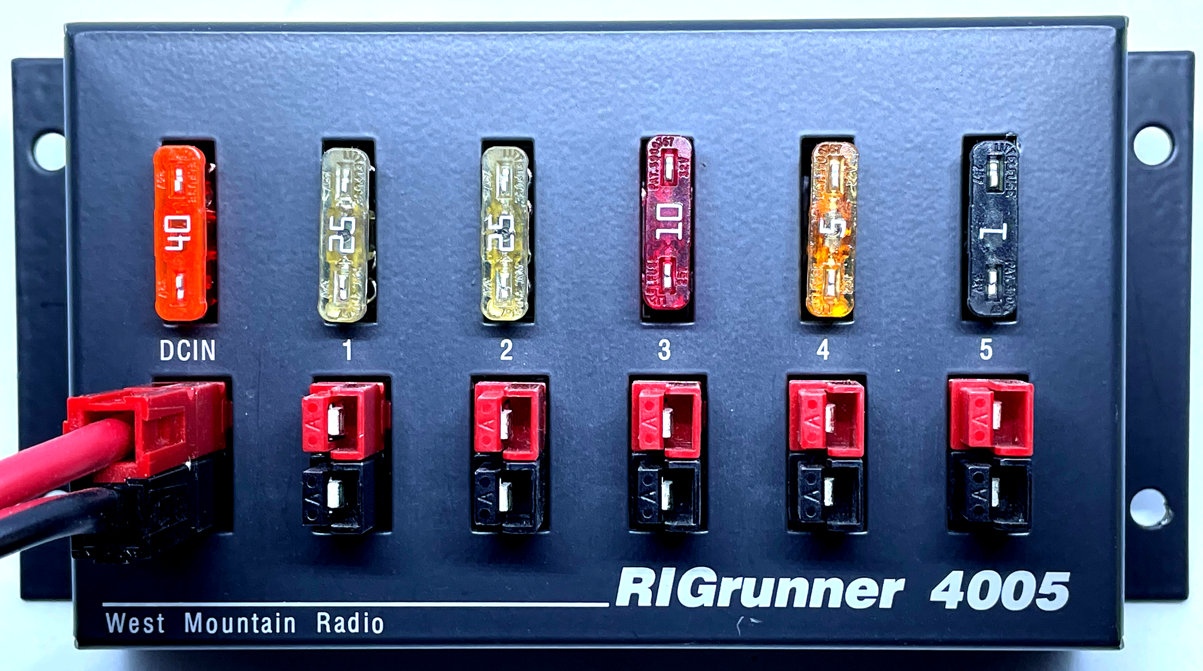 1) Kurzbeschreibung: Anschlussbox eines Gleichstrom-Stromverteilers „RIGrunner 4005“ mit einem Eingang und fünf Ausgängen, jeweils bestückt mit Kfz-Stecksicherungen.

2) Ausführliche Beschreibung: Das Foto zeigt die Anschlussbox eines Gleichstrom-Stromverteilers „RIGrunner 4005“ des Unternehmens „West Mountain Radio“. Die Box besitzt nebeneinander einen Eingang („DCIN“) und fünf Ausgänge („1“ bis „5“). In der Eingangsbuchse steckt ein Anschlussstecker mit einem roten und einem schwarzen Gehäuse. Die Ausgänge bestehen aus Anschlussbuchsen, ebenfalls mit einem roten und einem schwarzen Gehäuse. Über dem Eingang und den Ausgängen sind jeweils Kfz-Stecksicherungen unterschiedlicher Farbe und mit unterschiedlicher Beschriftung zu sehen.