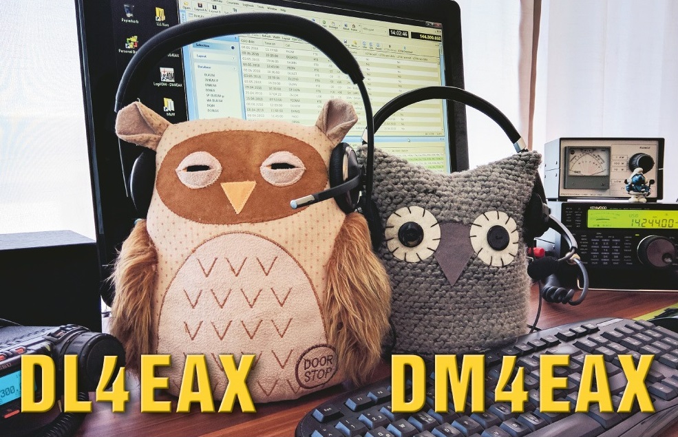 Der folgende Alt-Text wurde noch nicht geprüft: Zusammenfassung: Zwei Eulen‑Stofftiere mit Headsets sitzen vor einem Funkarbeitsplatz mit Monitor, Tastatur und Funkgeräten; am Bildrand sind groß die Rufzeichen „DL4EAX“ und „DM4EAX“ eingeblendet.

Detaillierte Beschreibung: Auf einem Holztisch stehen zwei Eulen-Plüschfiguren nebeneinander, beide tragen schwarze Kopfbügel-Headsets mit Mikrofonarmen. Die linke Eule ist beige-braun mit applizierten Flügeln und einem runden Label „DOOR STOP“ am Bauch, die rechte Eule ist grau gehäkelt mit großen, runden Augen. Dahinter stehen zwei große Monitore; auf dem mittigen Bildschirm ist ein Fenster mit tabellarischer Liste und Spalten zu sehen. Rechts auf dem Tisch befindet sich ein schwarzer Transceiver mit digitaler Anzeige und Drehknöpfen, daneben ein kleines analoges Messgerät mit Zeiger; darauf steht eine kleine blaue Figur. Vorne liegt eine schwarze Computertastatur, mehrere Audiokabel verlaufen über den Tisch. Links unten ist der Rand eines weiteren Funkgeräts oder Mikrofons zu sehen. Im Hintergrund fällt Tageslicht durch helle Vorhänge. Unten im Bild sind in gelber, fetter Schrift die Texte „DL4EAX“ (links) und „DM4EAX“ (rechts) eingeblendet.