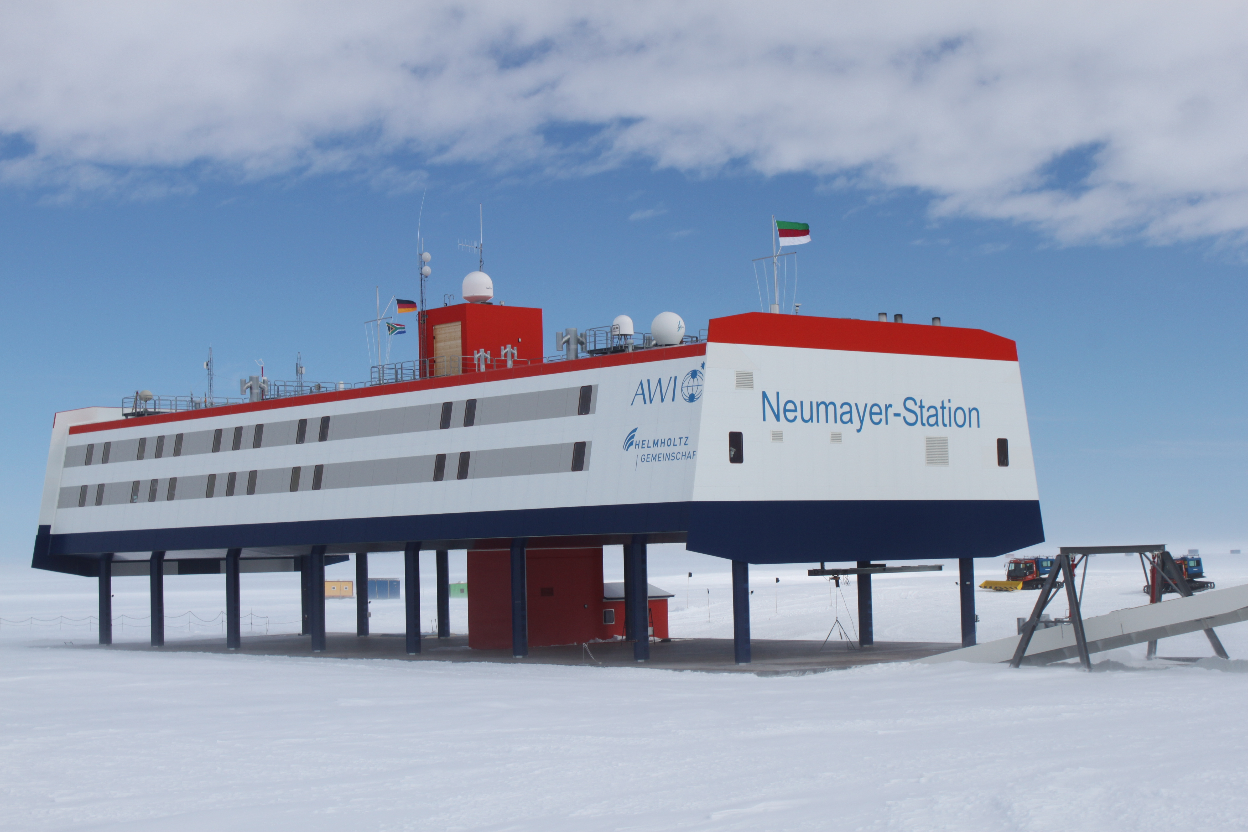 1) Kurzbeschreibung: Neumayer-Station in der Antarktis; langes, auf Stützen stehendes, weiß und grau gestreiftes Stationsgebäude mit rot abgesetzter Dachpartie und mit der Aufschrift „Neumayer-Station“ an der Stirnseite; auf dem Dach mehrere Masten, Antennen und Radome.

2) Ausführliche Beschreibung: Das Foto zeigt die deutsche Neumayer-Station in der Antarktis. Das rechteckige Stationsgebäude ist weiß und grau gestreift, hat eine rot abgesetzte Dachpartie und steht erhöht auf vielen dunklen Stützen. An der Stirnseite steht in großen Buchstaben „Neumayer-Station“. Auf dem Dach befinden sich ein roter Aufsatz und mehrere Stabantennen, Maststrukturen und mehrere weiße Radome.