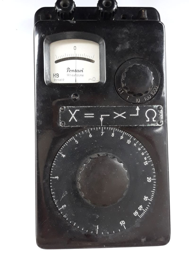 Der folgende Alt-Text wurde noch nicht geprüft: 1) Kurze Zusammenfassung: Schwarzes Messgerät mit analogem Zeigerinstrument, großem Drehring, zusätzlichem Drehschalter und mehreren Anschlussklemmen.

2) Detaillierte Beschreibung: Das Gerät hat ein rechteckiges, schwarzes Gehäuse und liegt auf weißem Untergrund. Oben links befindet sich ein rechteckiges Analoginstrument mit gebogener Skala und der mittigen Markierung „0“; auf der Skalenfläche steht „Pontavi Wheatstone“ sowie ein Ω-Symbol. Oben am Rand sitzen zwei schwarze Schraubklemmen; rechts oben sind zwei kleine, stiftartige Anschlüsse zu sehen. Rechts neben dem Messwerk ist ein kleinerer Drehschalter mit Skalenring, beschriftet mit 0,1 – 1 – 10 – 100 – 1000. Unterhalb des Messwerks ist eine schmale Metallplakette mit der Aufschrift „X =“ und Symbolen sowie einem Ω-Zeichen verschraubt. Den unteren Bereich dominiert ein großer, runder Drehring mit feiner Teilung und Zahlen von 0 bis 50 (in 5er-Schritten markiert), in dessen Mitte ein griffig ausgeformter Drehknauf sitzt. Das Gehäuse zeigt leichte Kratzer und Gebrauchsspuren; mehrere Schrauben sind sichtbar.