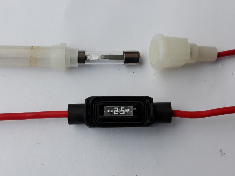 Der folgende Alt-Text wurde noch nicht geprüft: 1. Zusammenfassung: Zwei in rote Leitungen integrierte Sicherungshalter auf weißem Hintergrund, oben ein geöffneter mit Glasrohrsicherung, unten ein geschlossener schwarzer Halter mit Sichtfenster und der Aufschrift „2.5“.

2. Detaillierte Beschreibung: Auf einer weißen Fläche liegen zwei Abschnitte roter Kabel mit Zwischengehäusen. Oben ist ein weißer, zylindrischer Kunststoffhalter geöffnet: links das durchscheinende Rohrteil, rechts die abschraubbare Kappe mit angesetztem roten Kabel; dazwischen eine zylindrische Glasrohrsicherung mit metallischen Endkappen. Unten verläuft ein zweites rotes Kabel durch ein schwarzes, rechteckiges Inline-Gehäuse mit abgerundeten Kanten; in einem transparenten Fenster ist eine kleine Sicherung sichtbar, auf der weiß die Ziffern „2.5“ stehen. Beide Kabel treten jeweils links und rechts aus den Gehäusen aus.